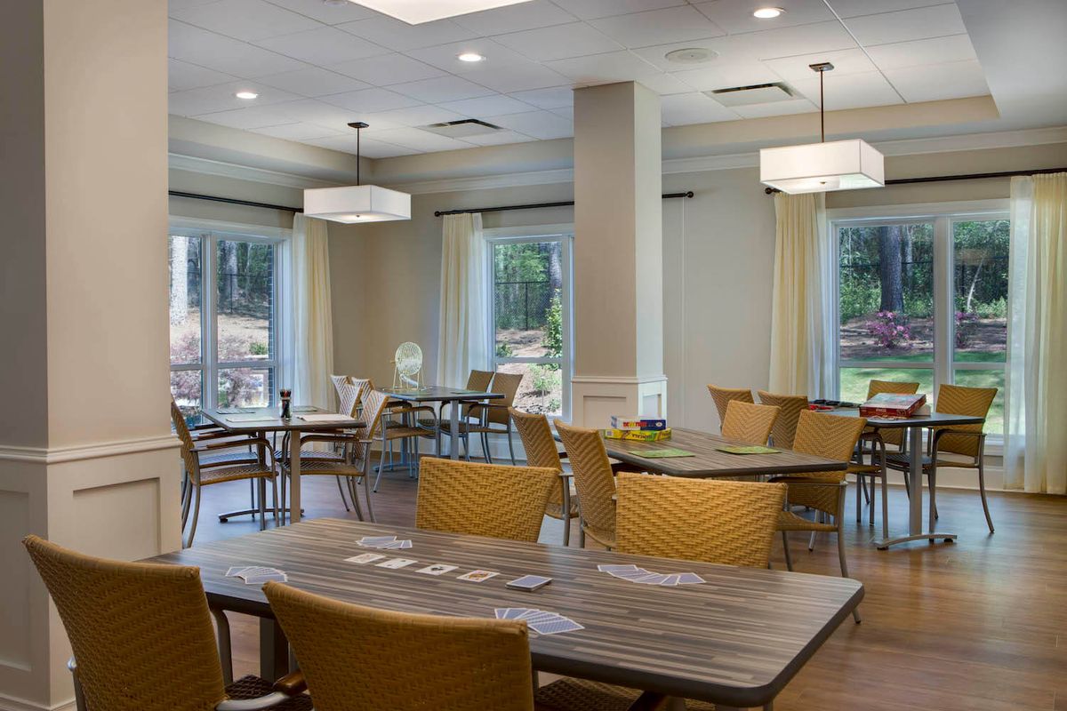 A modern dining area with multiple tables and chairs, illuminated by natural light through large windows.