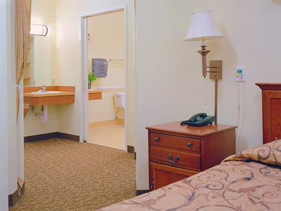 A cozy hotel room featuring a bed, nightstand with a lamp and telephone, and an adjoining bathroom.