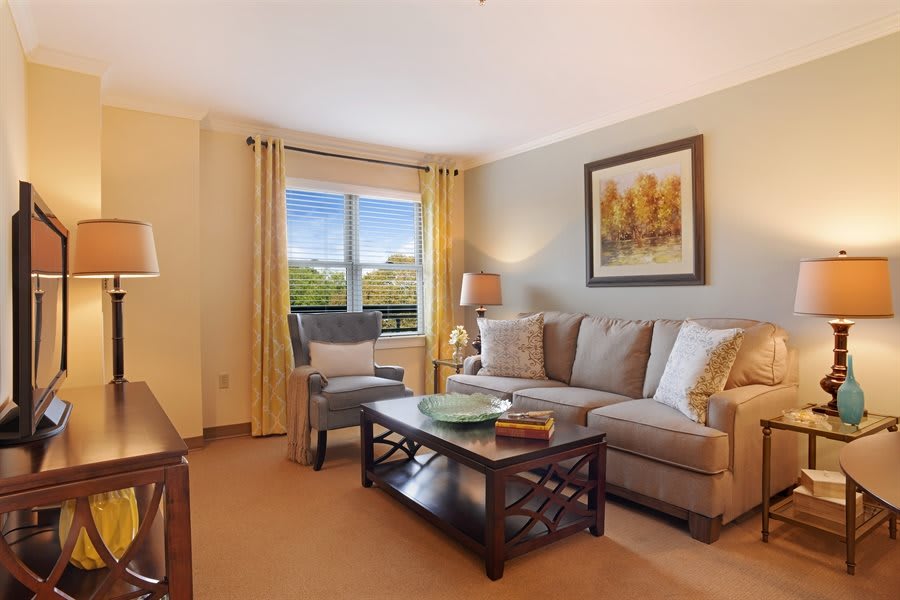 A cozy living room with a comfortable sofa and armchair, featuring a coffee table and large window with curtains.