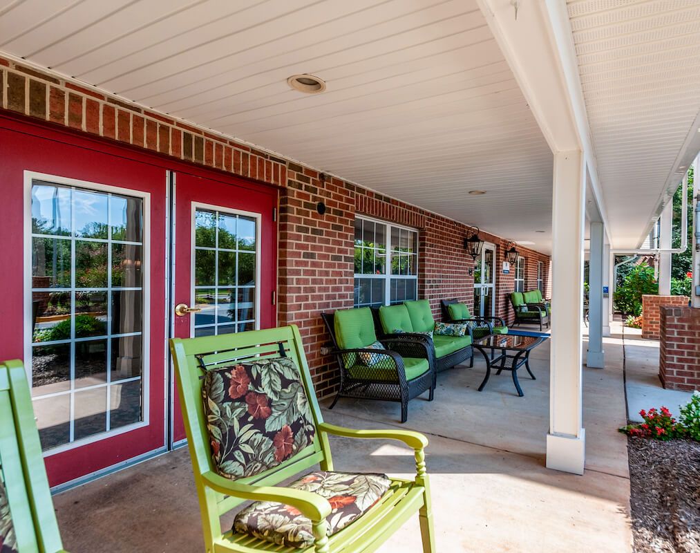 A cozy porch with colorful chairs and red doors against a brick wall.