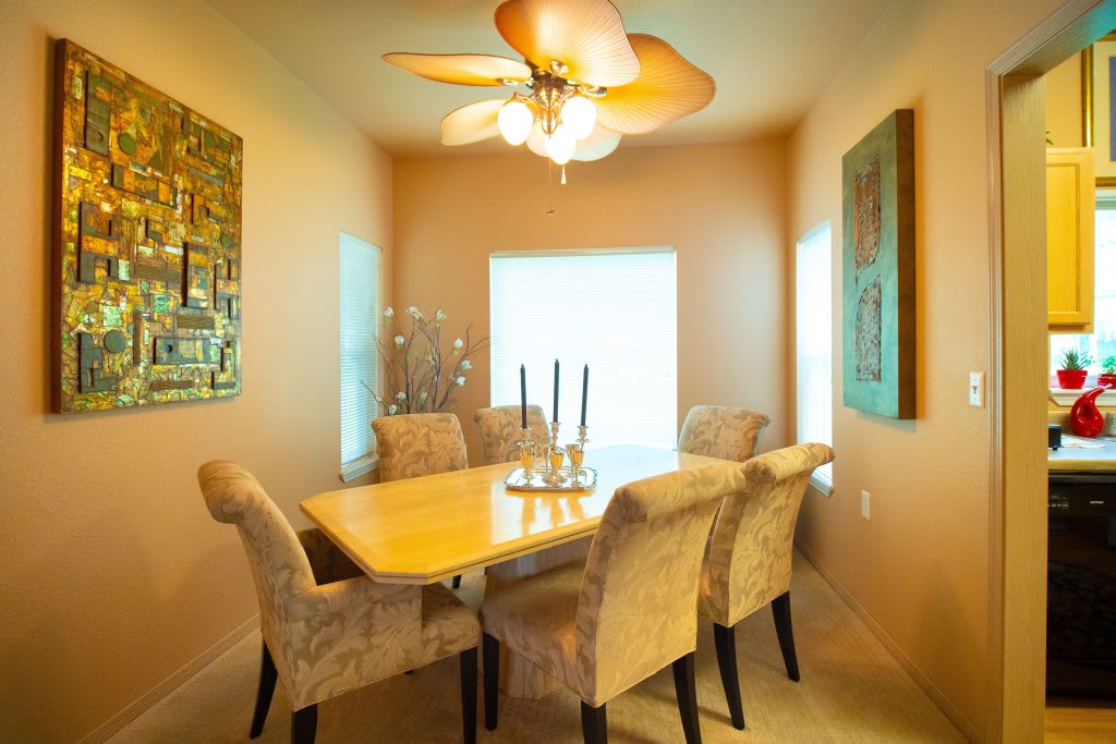 A cozy dining area with upholstered chairs around a wooden table, illuminated by a ceiling chandelier and adorned with wall art.
