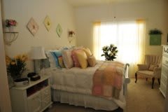 A cozy bedroom with a neatly made bed, colorful pillows, and soft lighting from a window.