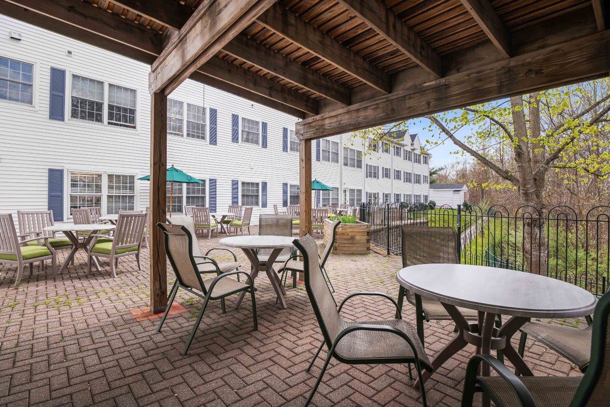 A covered outdoor patio area with tables and chairs, adjacent to a building with multiple windows.