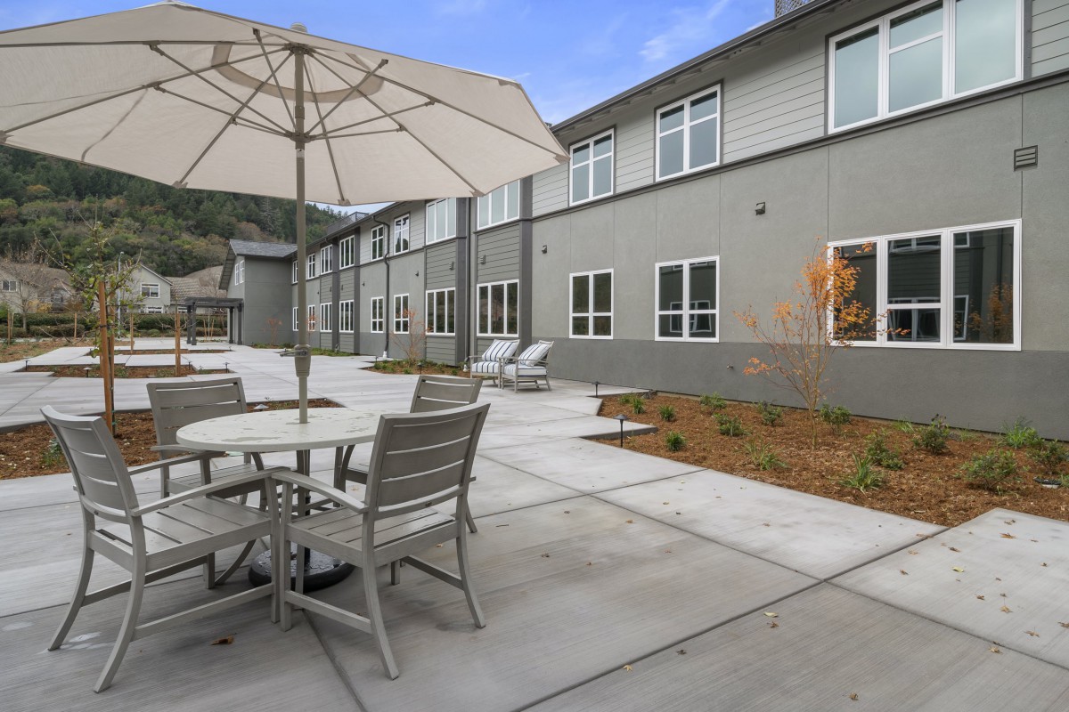 A modern outdoor patio area with tables, chairs, and an umbrella next to a building.