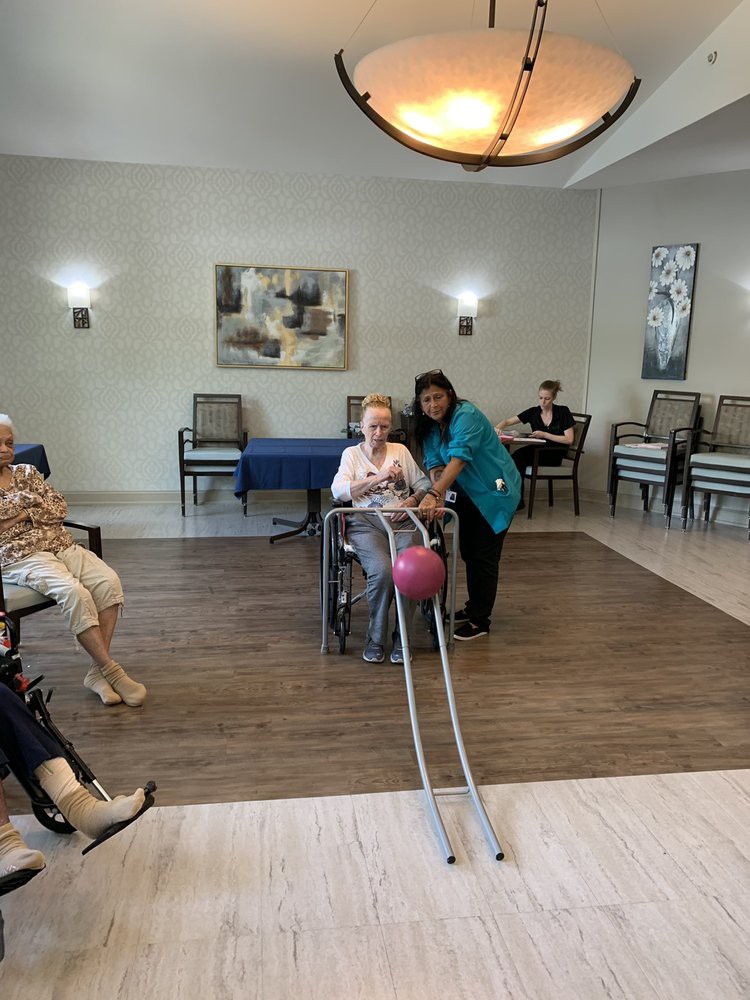 Elderly residents enjoy an indoor bowling activity with a caregiver's assistance.