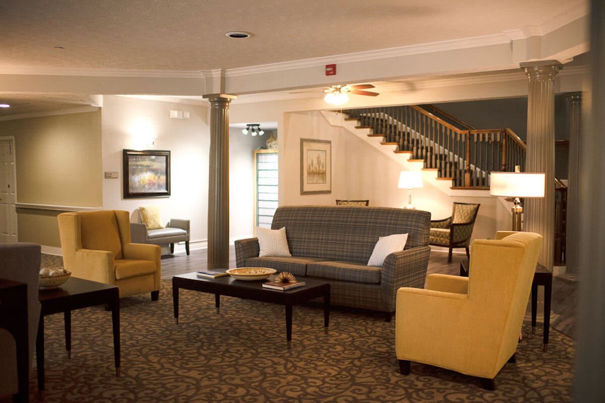 A cozy lobby area featuring a sofa, armchairs, and a central coffee table, with a staircase leading upstairs.