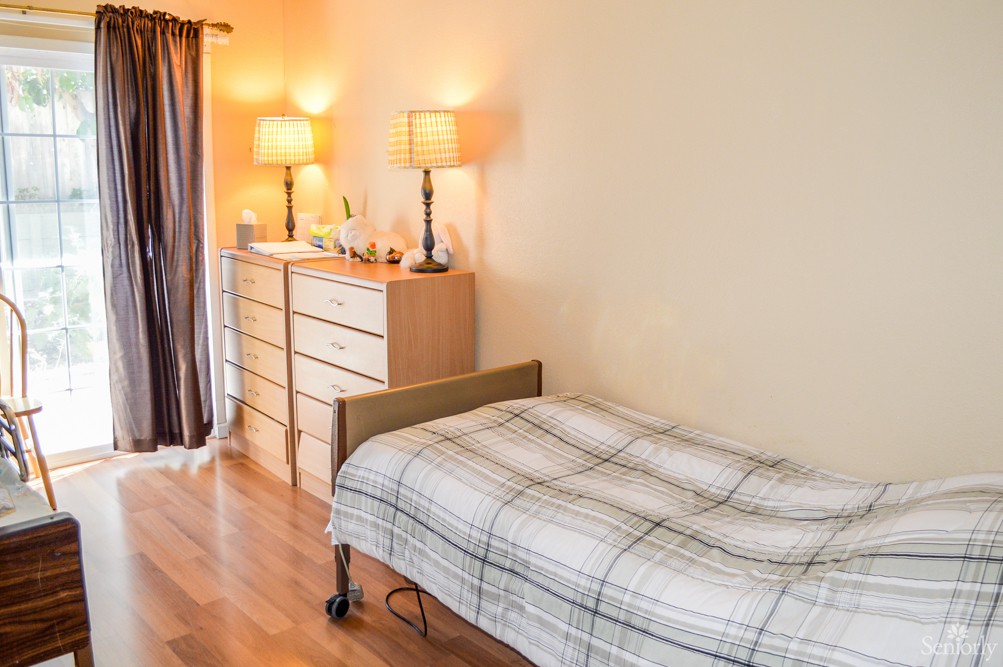 A cozy bedroom with a single bed, dresser, and warm lighting.
