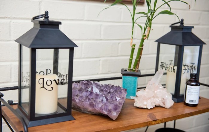 A cozy home decor setup featuring lanterns with candles, amethyst and clear crystals, and a bamboo plant.