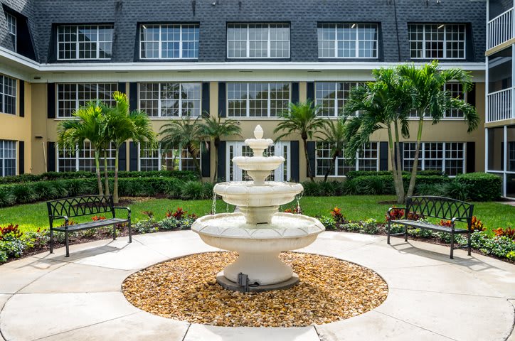 A beautifully landscaped courtyard featuring a central tiered fountain surrounded by palm trees and a well-maintained garden.