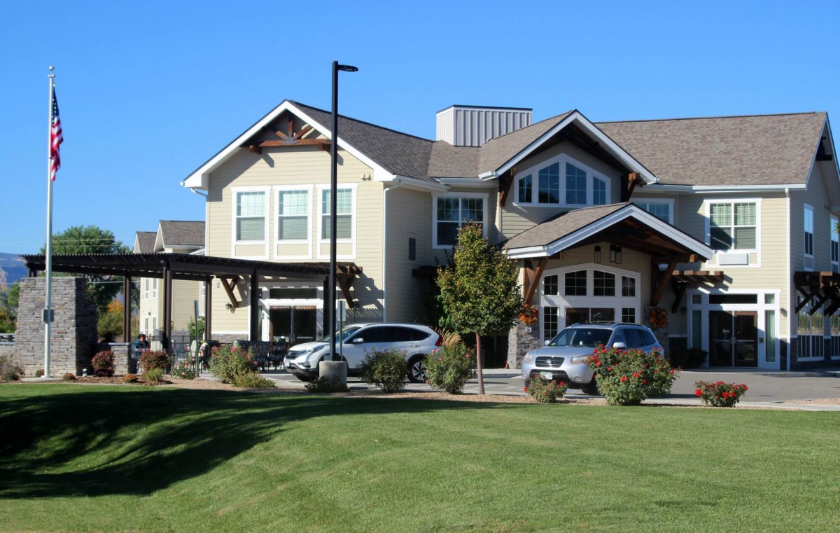 A modern residential building with parked cars and a grassy landscape.