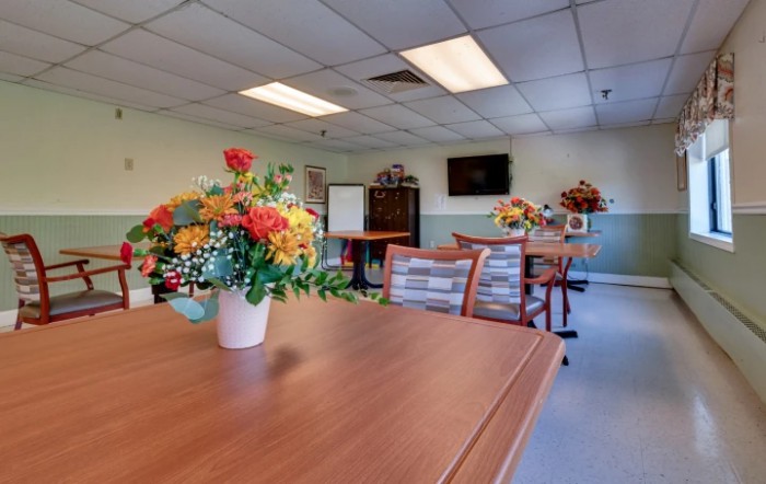 A well-lit room with tables and chairs, decorated with colorful flower arrangements.