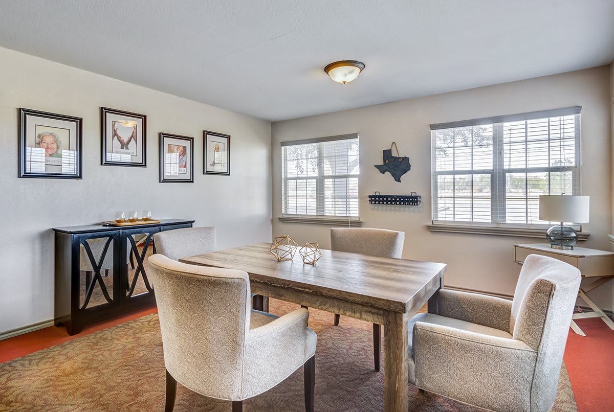 A cozy dining room with a wooden table and plush chairs, featuring decorative wall art and large windows that brighten the space.