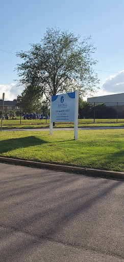 A sign outside a facility, surrounded by green grass and trees under a clear sky.