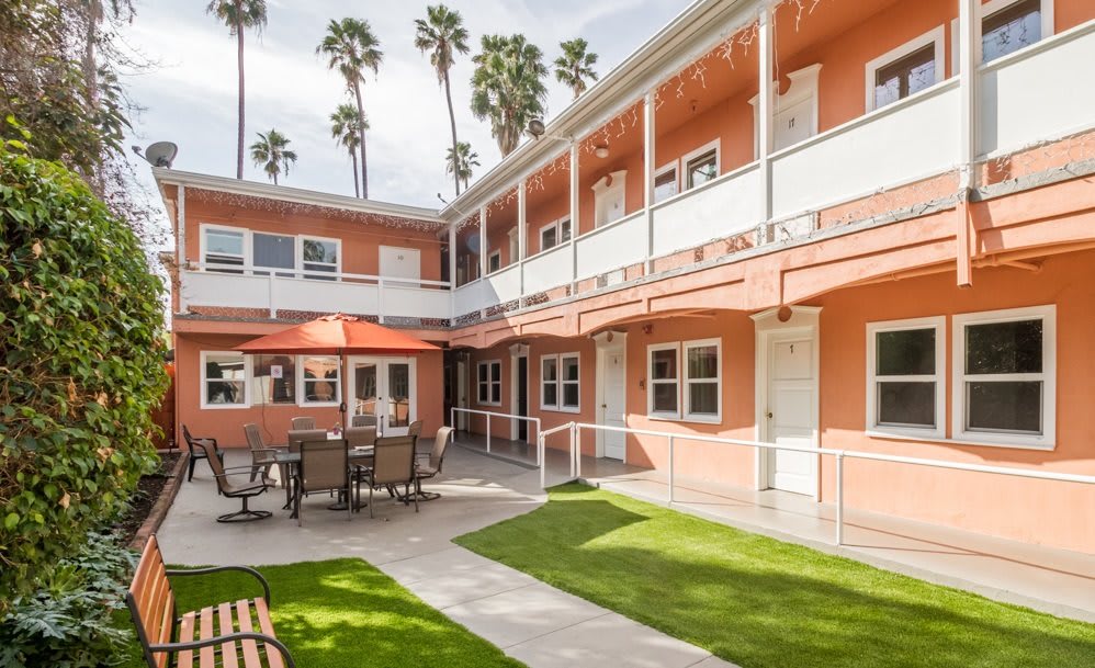 A charming courtyard with outdoor seating, surrounded by a two-story building and lush palm trees.