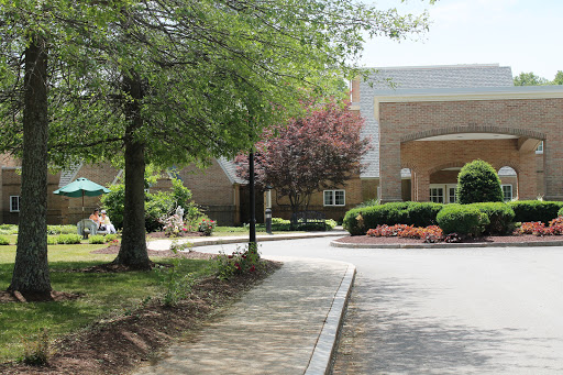 A peaceful scene featuring a pathway leading to a building surrounded by trees and landscaped gardens.