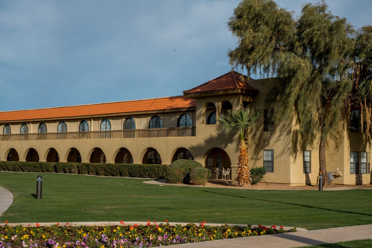 A two-story building with Spanish-style architecture surrounded by a well-maintained garden and palm trees.