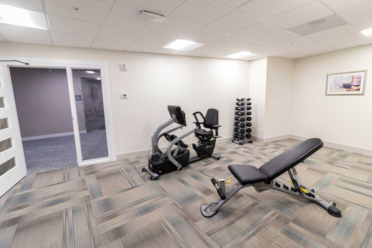 A small gym with a stationary bike, dumbbell rack, and workout bench.