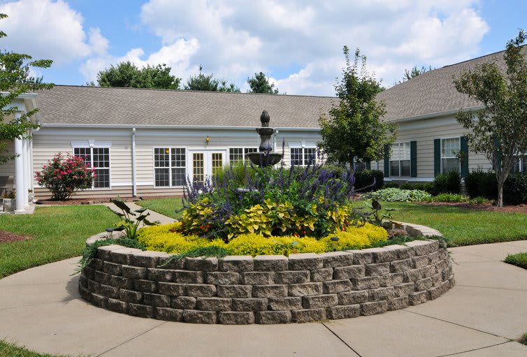 A beautifully landscaped garden with a central fountain and surrounding flower bed outside a building.
