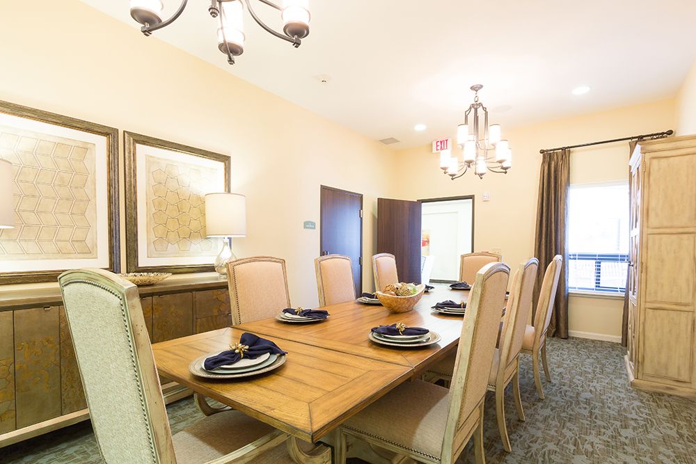 A well-decorated dining room with a wooden table and upholstered chairs, featuring elegant lighting fixtures.