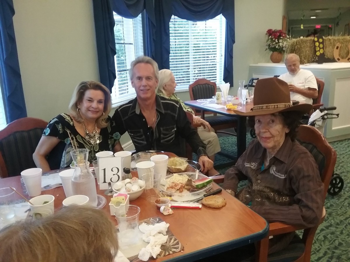A group of people enjoying a meal together, with one wearing a large hat, in a cozy dining setting.