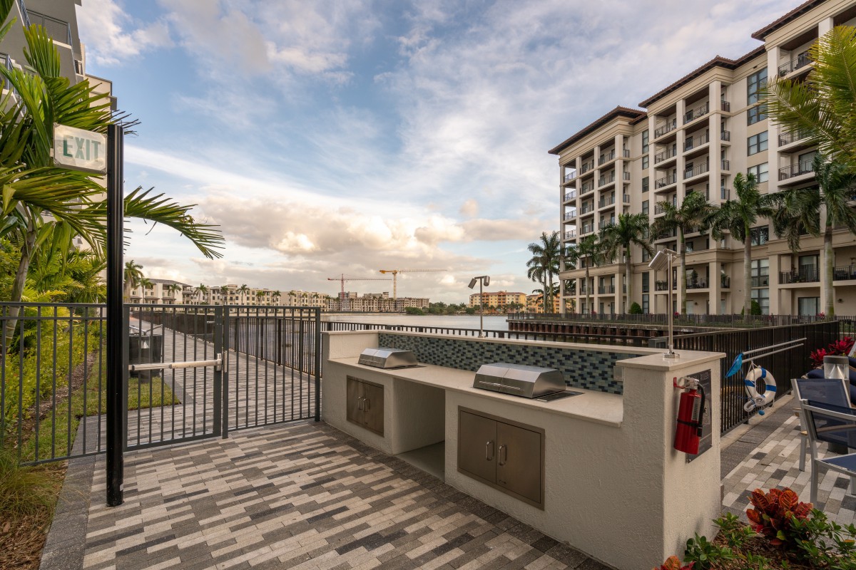 A modern apartment complex with an outdoor grill area overlooking a waterfront under a cloudy sky.