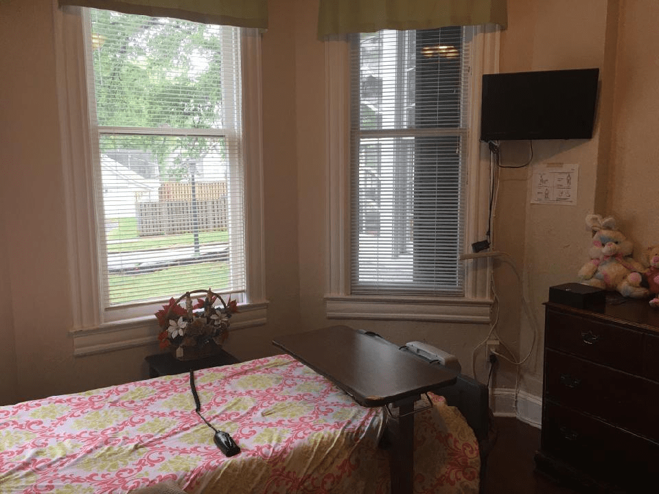 A cozy room with a single bed, a wall-mounted TV, and large windows offering natural light.