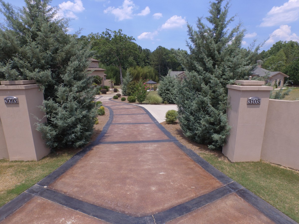 A neatly paved driveway lined with trees and landscaping elements.