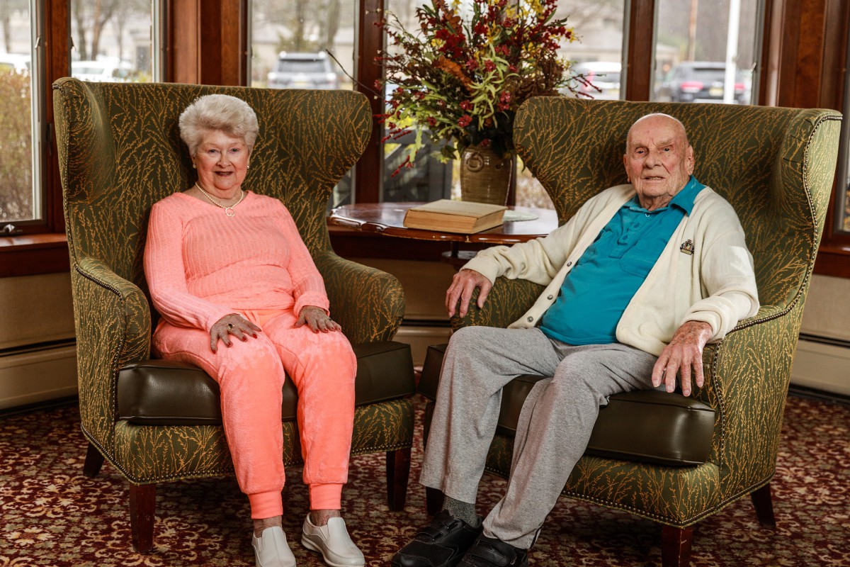 An elderly couple sitting on chairs in a cozy living room setting.