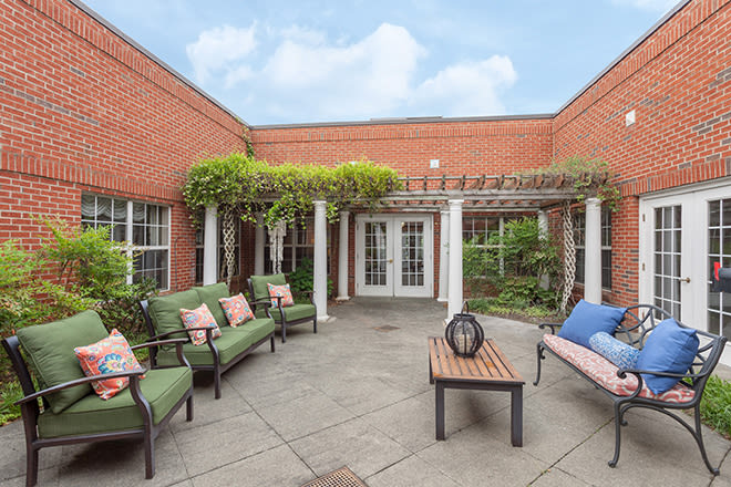 A cozy courtyard with green-cushioned seating, a wooden bench, and a pergola adorned with plants.