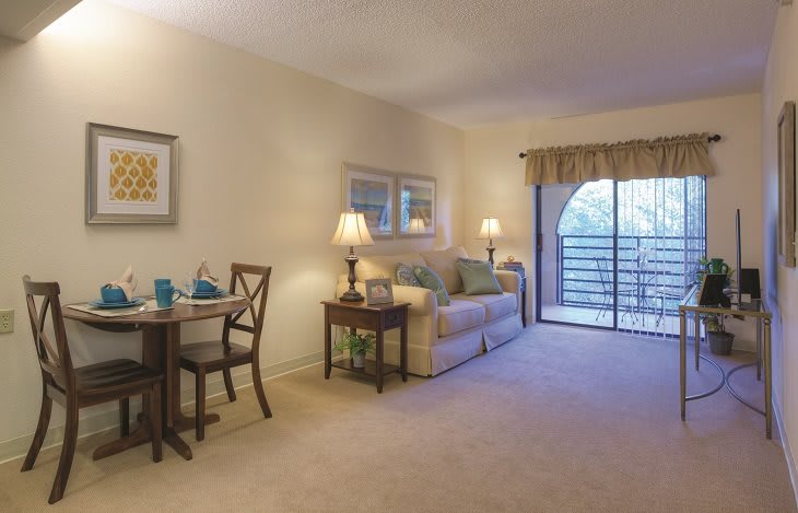 A cozy living room with soft lighting, featuring a sofa, dining table, and sliding glass doors leading to a balcony.
