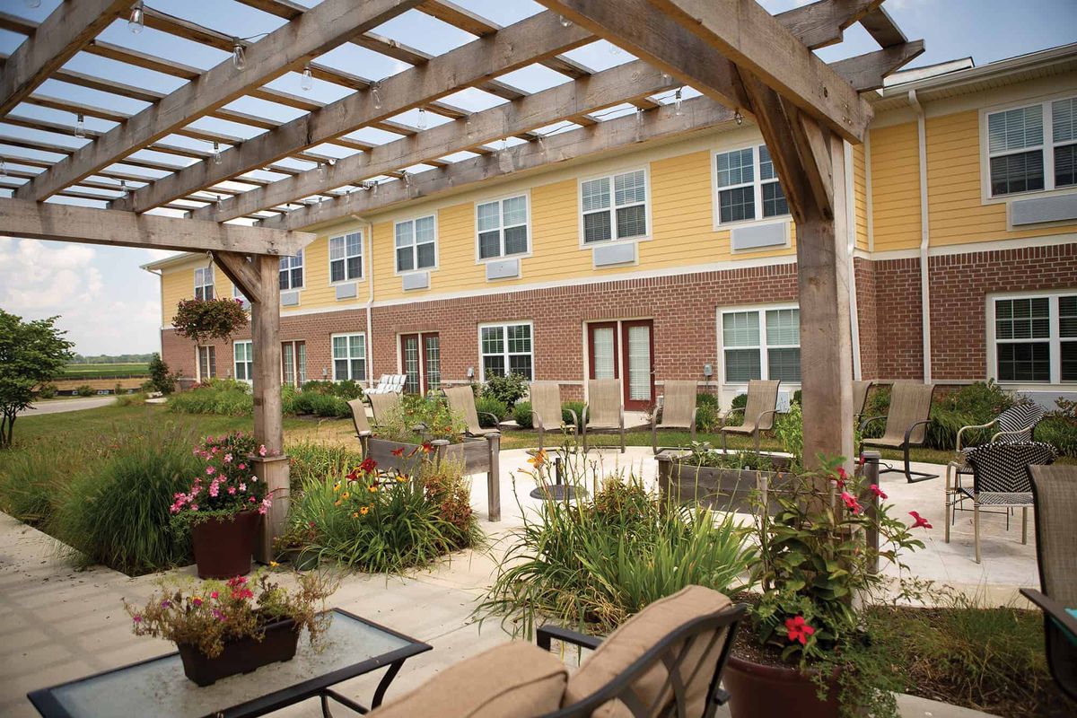A beautifully landscaped garden patio with outdoor seating and a pergola, adjacent to a multi-story building.