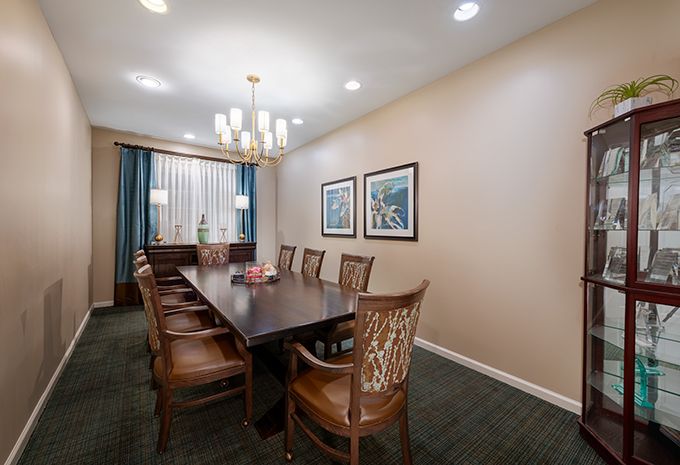 A well-lit dining room with a long wooden table, several chairs, and two framed artworks on the wall.