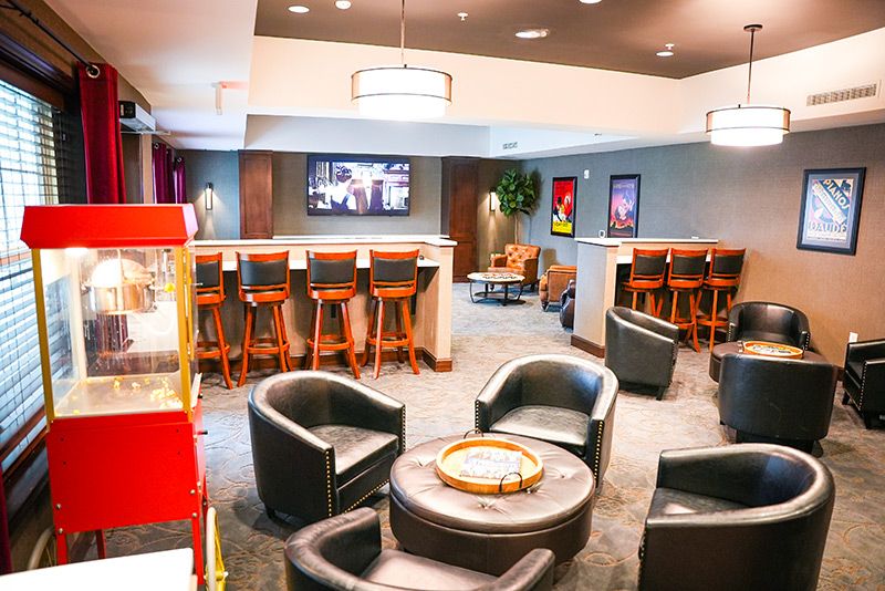 A cozy lounge area featuring black leather chairs, bar stools, a television, and a popcorn machine.