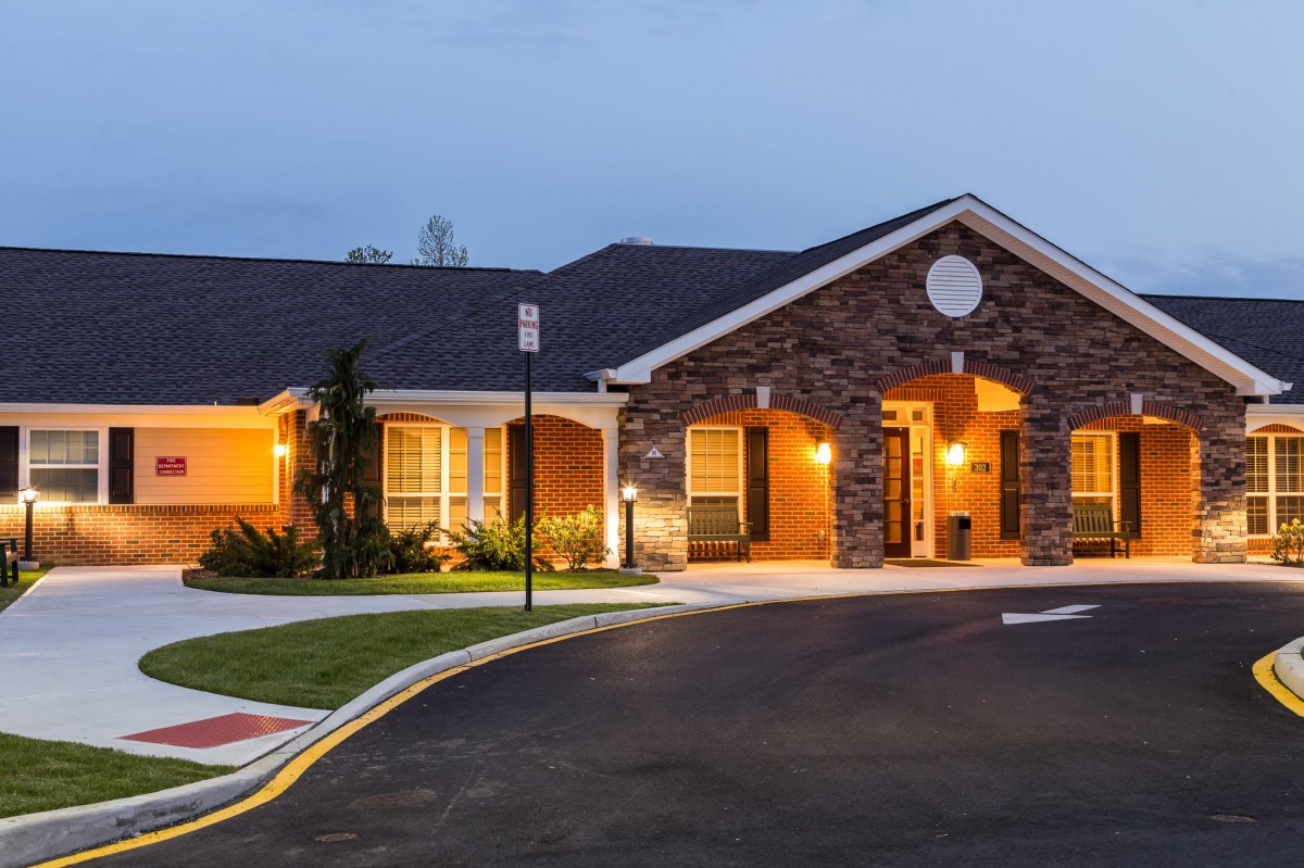 A well-lit residential building with a stone facade and a driveway, captured during the evening.