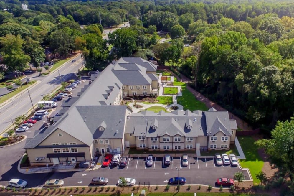 Aerial view of a large building complex surrounded by trees, with a parking lot in the front.