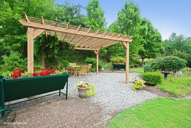 A serene garden with a wooden pergola and outdoor seating area surrounded by lush greenery.