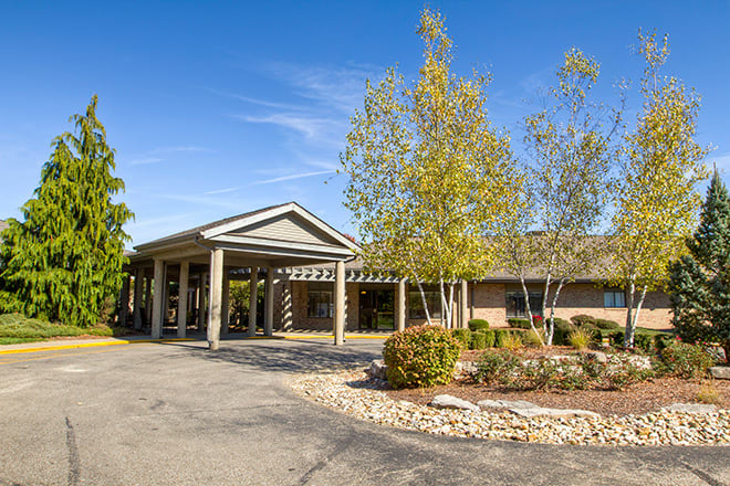 A building entrance surrounded by trees and landscaping under a clear blue sky.