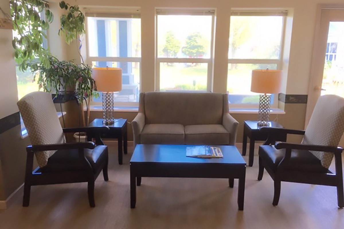 A cozy living room with a sofa, chairs, and coffee tables by large windows.