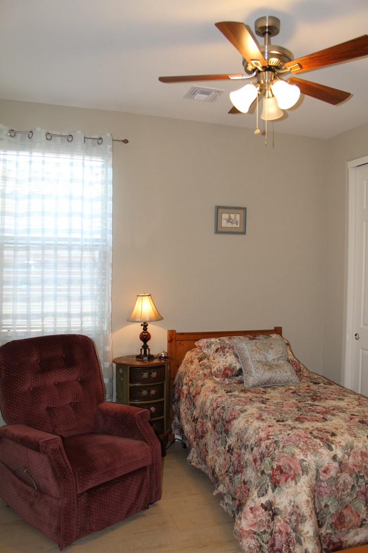 A cozy bedroom with a single bed, an armchair, and a bedside lamp under a window.