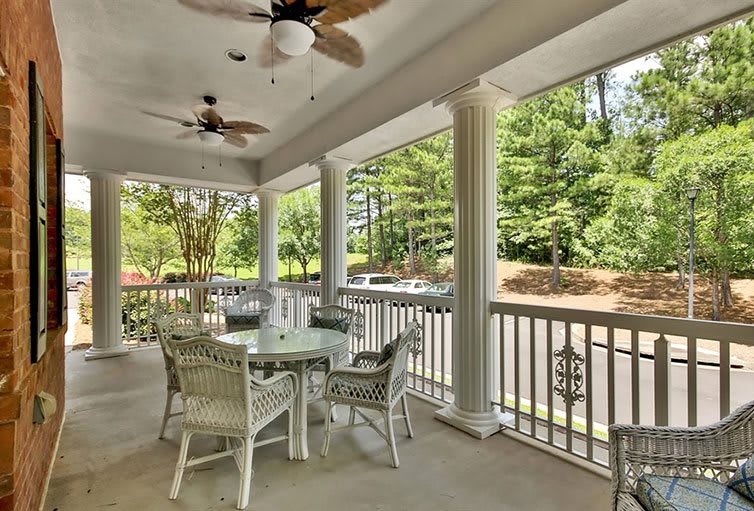 A cozy porch with wicker furniture and ceiling fans overlooking a wooded area.