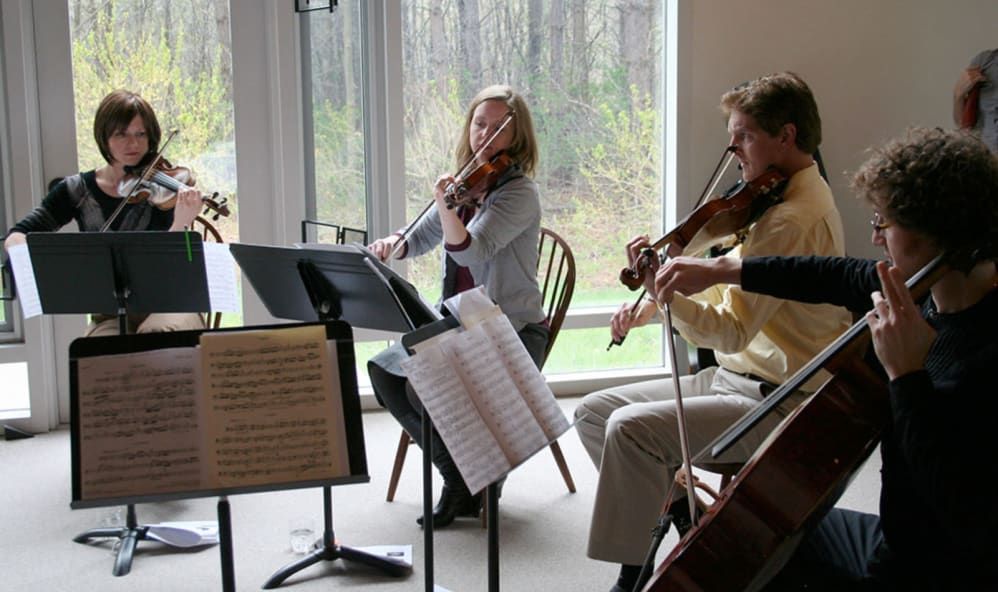 A string quartet rehearsing indoors with sheet music in front of them.