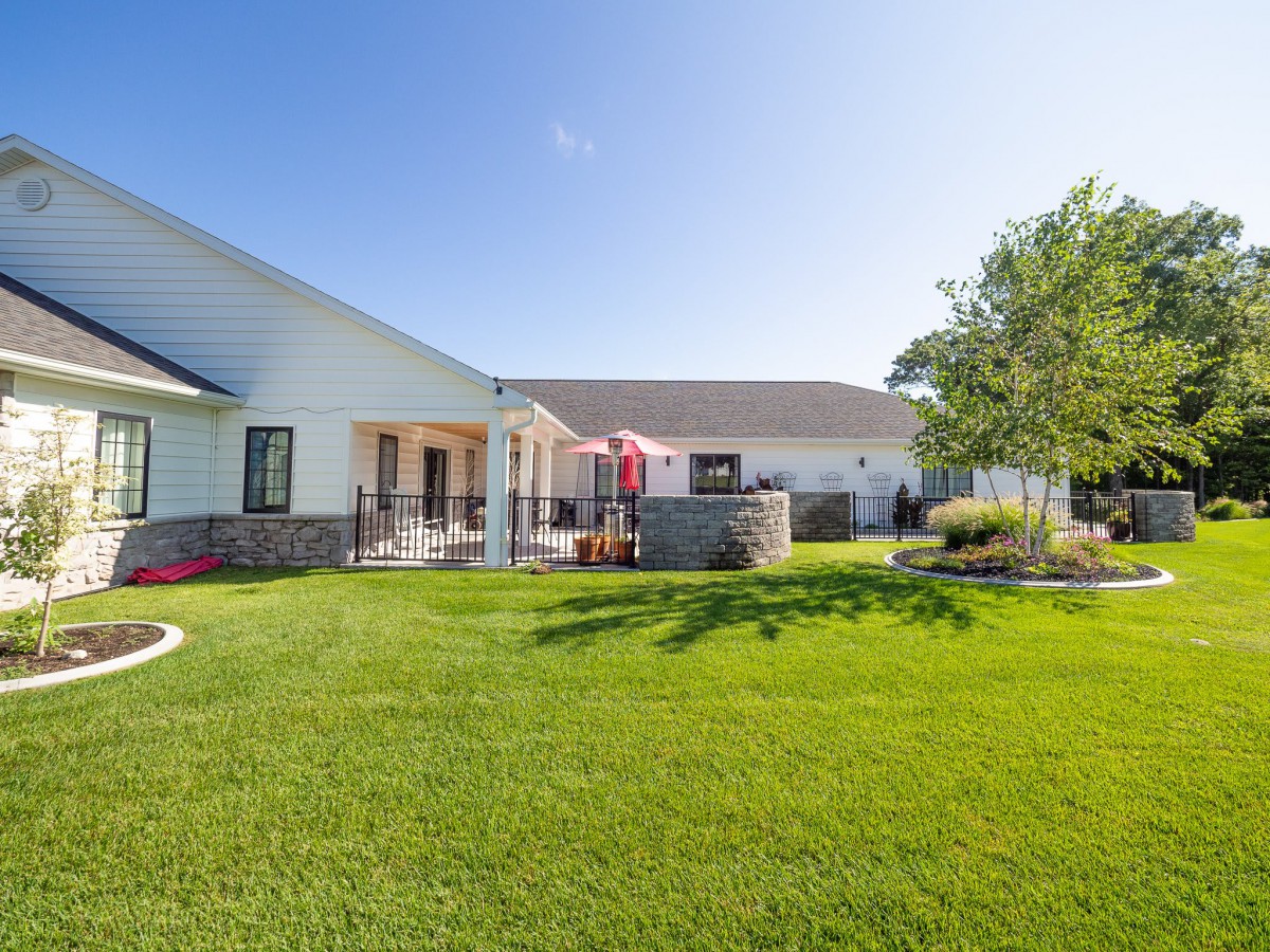 A spacious backyard with a well-maintained lawn, patio area, and trees under a clear blue sky.