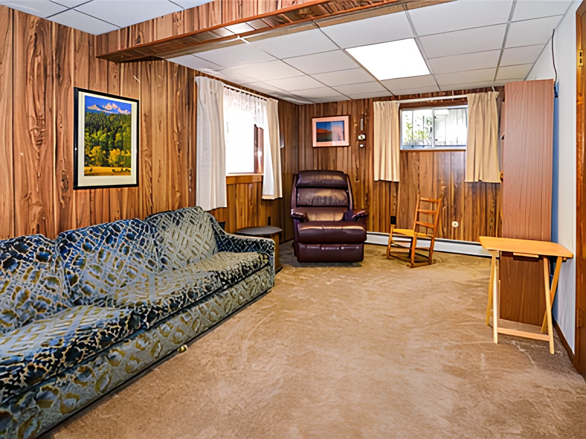 A cozy basement living room with wood paneling, featuring a couch, armchair, and framed artwork on the walls.