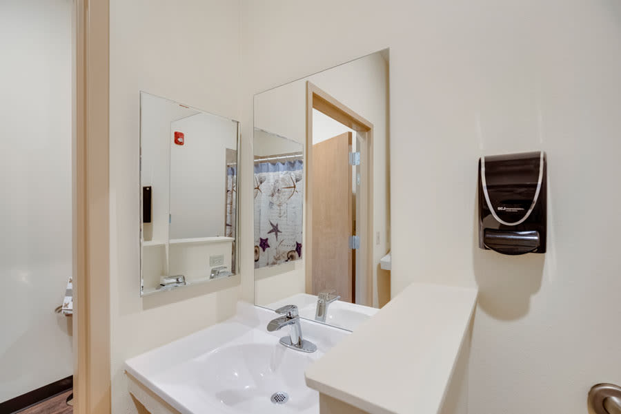 A modern bathroom with a sink, mirror, and towel dispenser.