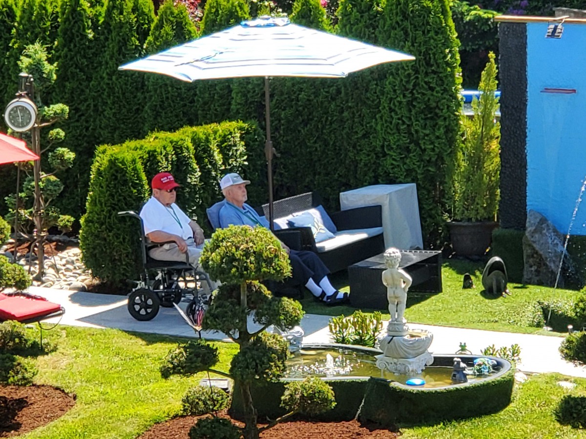 Two people relax in a beautifully landscaped garden with a fountain and an umbrella providing shade.