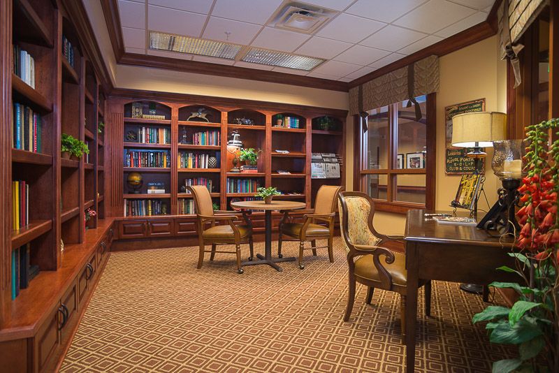 A cozy library with wooden bookshelves, comfortable chairs, and a central table for reading or study.