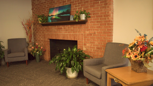 A cozy living room corner featuring a brick wall, a fireplace, potted plants, and a comfortable gray chair.