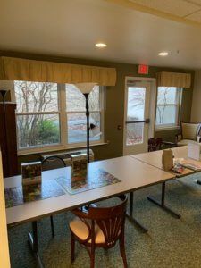 A meeting room with tables and chairs arranged near large windows with a lamp in the corner.