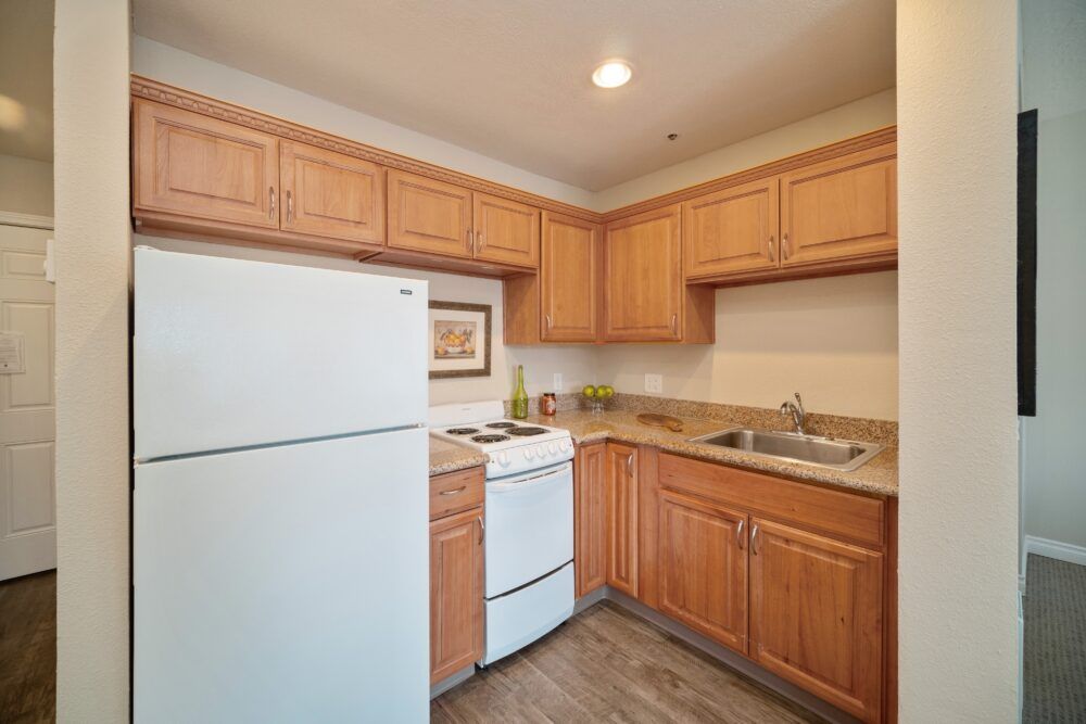 A small kitchen with wooden cabinets, a refrigerator, stove, and sink.