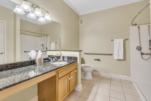 A modern bathroom with a granite countertop, large mirror, and tiled floor.